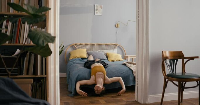 Girl in yellow top having fun and dancing around bed and lying on it during fun at home in cozy modern apartment. Cheerful girl improvises dance and dances in bedroom