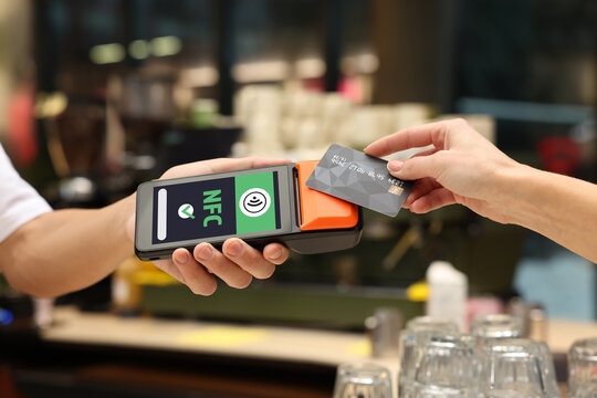 Payment terminal with NFC system. Client using credit card to pay for service in cafe, closeup
