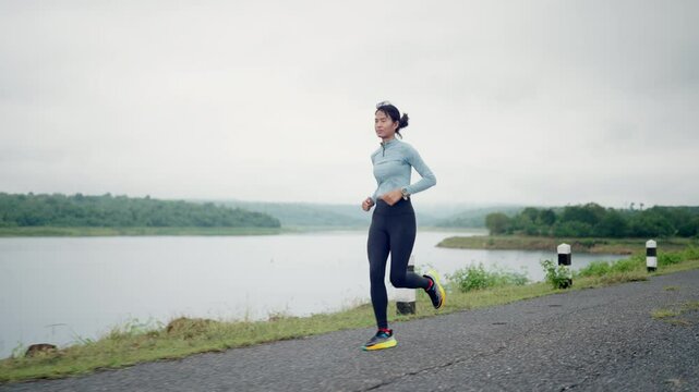 A woman is running on a road near a lake. She is wearing a blue shirt and black pants