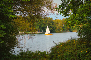 Lake scape with sailing boat, framed by green foliage and autumnal trees.