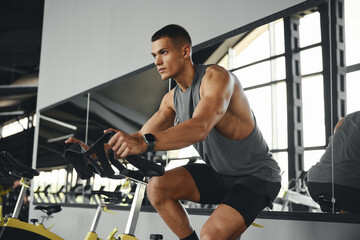 Fit young man in sportswear riding a stationary cycling bike in modern gym. Fitness and health care...