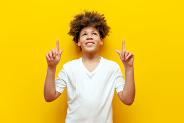 cheerful curly african american boy pointing finger up and smiling on yellow isolated background,...