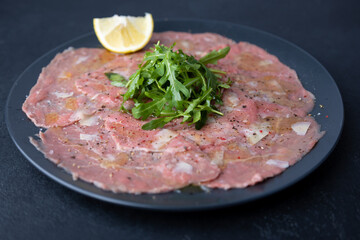Marbled beef carpaccio with arugula, parmesan cheese, olive oil and lemon. A traditional classic appetizer made from thinly sliced raw meat. Close-up, selective focus, black background.