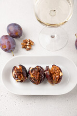 Plums baked with Camembert cheese, walnuts, honey and glass of white wine. Popular hot appetizer on a black plate. Selective focus, close-up.