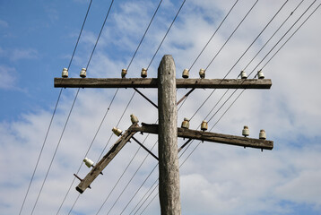 damaged old wooden power line pole against blue sky