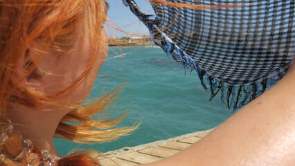 Redhead woman enjoys a breezy day at the beach, holding a checkered scarf.