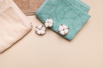 Cotton terry towels in neutral colors with cotton flowers on beige background. Natural eco-friendly fluffy material for hygiene, spa, bath procedures. Towel mockup top view flat lay