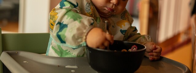 Fototapeta na wymiar Cute baby happily eating cereal. Perfect for family, food, and parenting blogs.