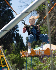 Happy little girl enjoying a bungee trampoline ride at an outdoor amusement park on a sunny day. She is smiling, mid-air, wearing casual clothes. Joyful childhood moment in action.