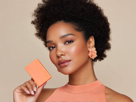 Elegant black woman with radiant skin holding orange soap bar, her voluminous hair and stylish earrings. image exudes confidence and beauty