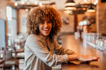 Fototapeta premium Smiling afro-haired businesswoman leaning on bar counter in restaurant