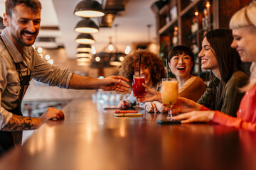 Bartender serving cocktails to happy female friends at bar counter