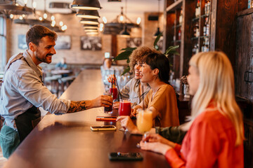 Bartender serving cocktails to happy female friends at bar counter