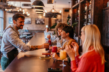 Bartender serving cocktails to happy female friends at bar counter
