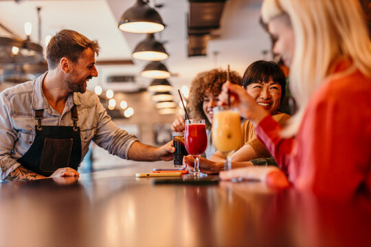 Bartender serving cocktails to happy female friends at bar counter