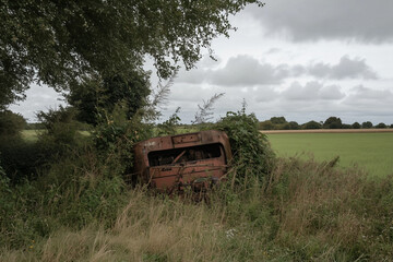 Naklejka premium Abandoned Vehicle Wreckage in a Field Under an Overcast Sky
