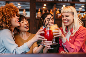 Cheerful multi-ethnic friends toasting cocktails at bar counter, enjoying nightlife