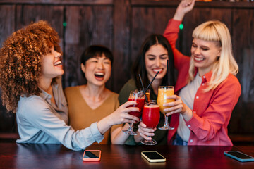 Cheerful female friends toasting cocktails in a pub