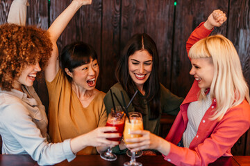 Cheerful multi-ethnic friends toasting cocktails, celebrating and having fun at the bar