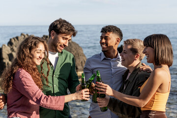 Happy diverse friends celebrating with beers by the sea during summer