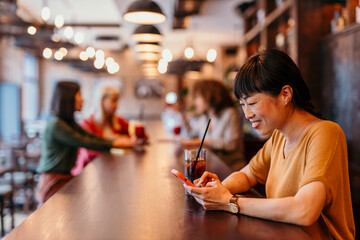 Woman using smartphone and drinking soda at bar counter in restaurant