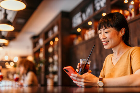 Smiling woman using smartphone and drinking soda in restaurant bar