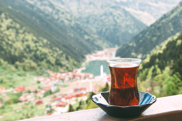 Traditional Turkish tea in a tulip-shaped glass with a scenic view of Uzungol lake and surrounding mountains in the Trabzon Karadeniz region of Turkey, concept of travel