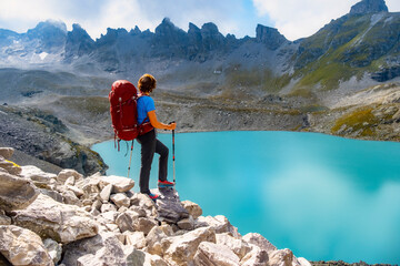 Hiker with a red backpack and poles admires the view of Pizol Lake Wildsee in a breathtaking...