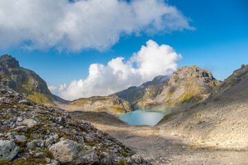 Captivating landscape of Pizol Wildsee lake in the Swiss Alps, featuring tranquil turquoise water amid rugged peaks enveloped by mist and clouds, creating a dramatic mountain scene
