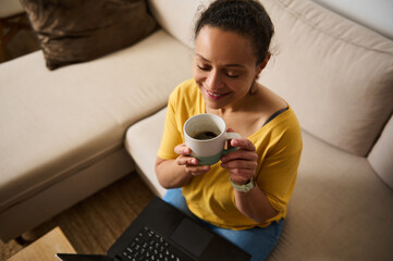 Relaxed Woman Enjoying Coffee While Working on a Laptop in a Cozy Home Setting