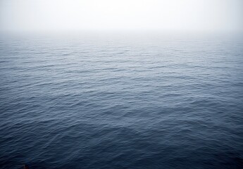 Obraz premium Vast, dark blue ocean, veiled in a light mist. Calm water surface, with gentle ripples. A distant, faint figure, barely visible