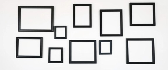 Empty black photo frames in varying sizes arranged on a plain white wall,  photography,  contemporary