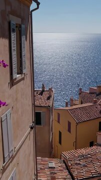 Sunlight reflects on the Mediterranean Sea near colorful houses with tiled roofs and bougainvillea in Roquebrune Cap Martin, France