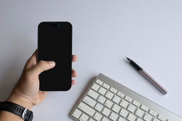 Top view of hands using smartphone on white desk with keyboard and pen
