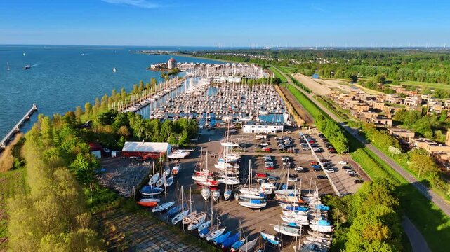 Approaching the boats on the shore near the parking lot. Numerous yachts stand on the anchor in yacht club. Green cityscape of Lelystad, the Netherlands at backdrop.
