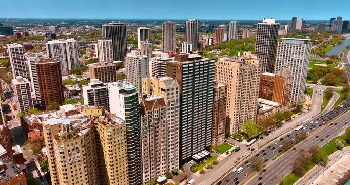 Approaching a row of high-rise buildings standing close to each other. Multiple cars go by the highways of Chicago, Illinois, USA.