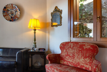 Living room finely decorated with classical-style furniture, with a black leather sofa, a red armchair and an elegant lamp