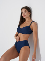 Obraz premium Smiling woman with long hair models a dark blue two-piece swimsuit, striking a confident pose. She accessorizes with small hoop earrings, enhancing her elegant appearance