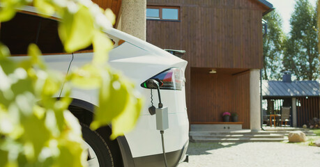 A white electric car charges at a home station in front of a luxury villa, symbolizing clean energy, Eco-friendly transportation, and sustainable living with modern green technology.