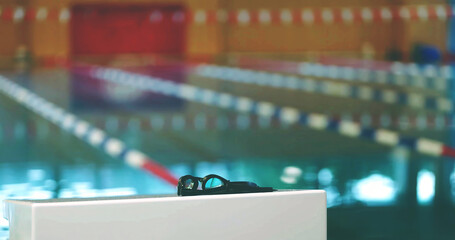 Swimming Goggles on Pool Launch Pad in Close-Up with Selective Focus and Swimming Pool Background
