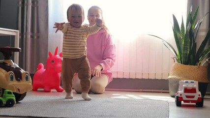 A joyous moment as a baby takes their first steps indoors, with a supportive adult close by, surrounded by toys.