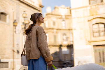 A woman smiles while looking up at historic architecture during a morning walk with her dog. The photo captures the essence of mindful travel, ideal for use in lifestyle, tourism, and wellness
