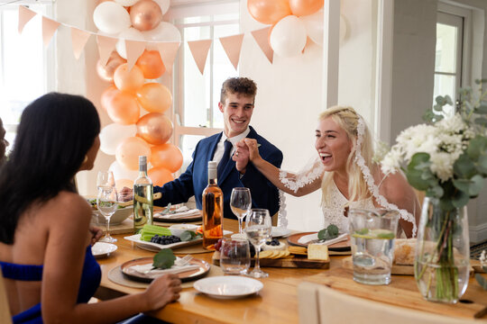 Bride and groom joyfully celebrating with friends at wedding reception table