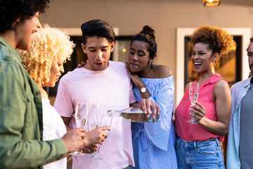 Obraz premium Young Diverse friends enjoying outdoor gathering, pouring champagne and laughing together