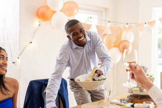 Smiling man serving salad at wedding celebration with friends raising glasses