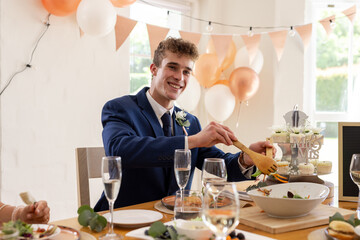 Smiling groom in suit serving food at wedding reception with festive decor