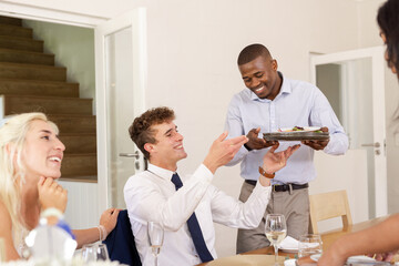 Diverse guests enjoying gourmet meal served by waiter during wedding celebration indoors