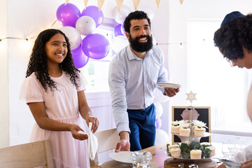 Diverse family celebrating religious event at home, setting table with smiles and joy