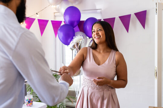 Diverse family, Smiling mother in pink dress handing gift card at festive celebration, at home - Powered by Adobe