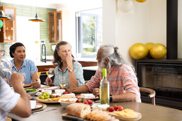 Around dining table, senior friends having wine and talking at home
